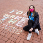 A student poses next to her chalk message along Campus Walk.