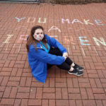 A student poses in front of her chalk message on Campus Walk.