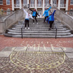 Volunteers pose on the front steps of Lee Hall during MLK Day of Service. A chalk drawing is visible on Campus Walk.