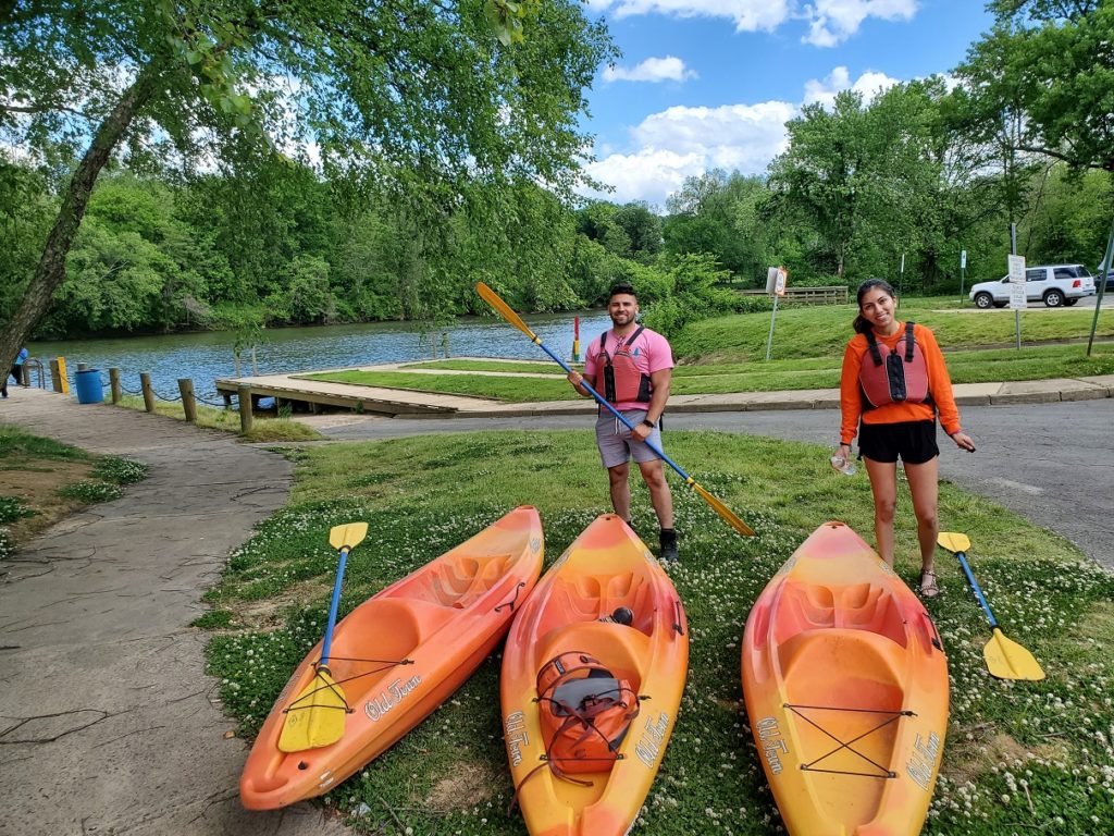 Two people stand by the river in front of three kayaks.