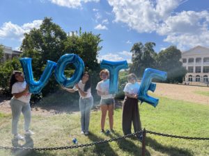 four students, each holding balloons, with letters that spell out "vote"