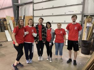six students in red t-shirts stand in a wearhouse
