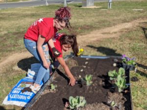 Two students wearing red shirts work in a garden.