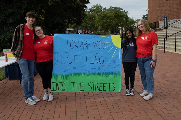 Four students in red shirts stand by a banner that asks "how are you getting into the Streets?"