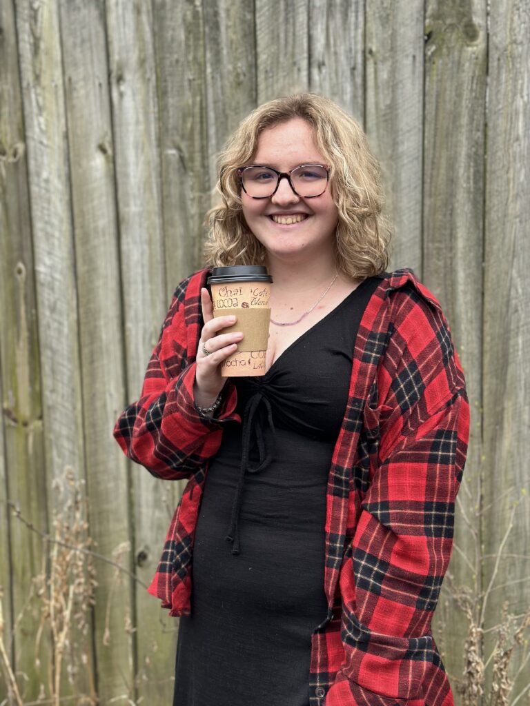 This is Emma holding a coffee with short blond hair and a flannel
