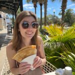 Picture of Emily Thomas, with blonde hair, sunglasses, and holding a crepe. 