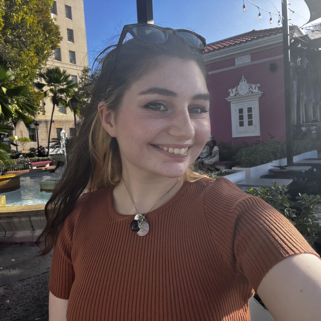 Sarah in a ribbed brown shirt, smiling cheerfully!