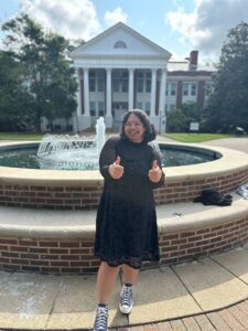 Student Amara Zavala standing in front of the Monroe foundation making the "thumbs up" sign. 