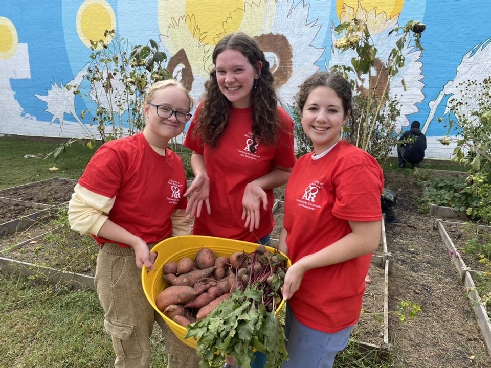 Students in red shirts show off the food they have harvested from a community garden.