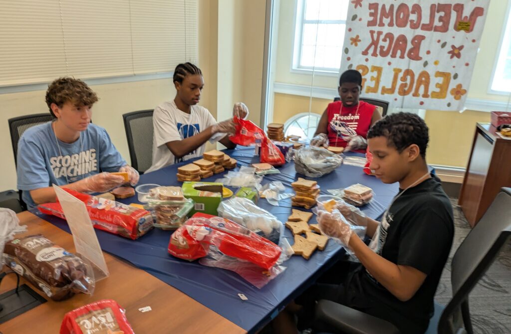 Four students prepare sandwiches with cheese. 