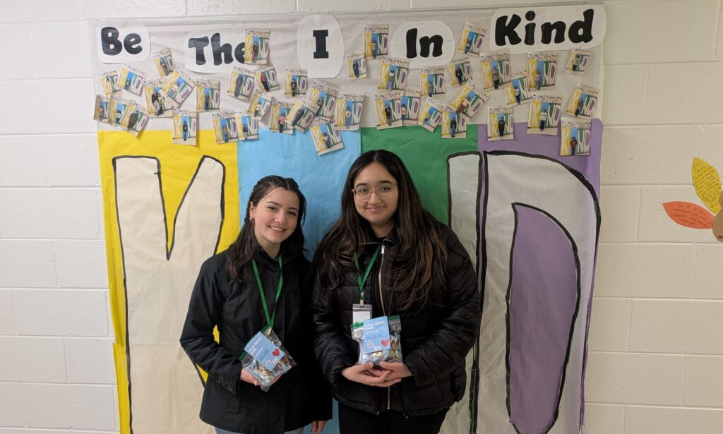two students stand in front of a sign that says be the "I" in KIND.