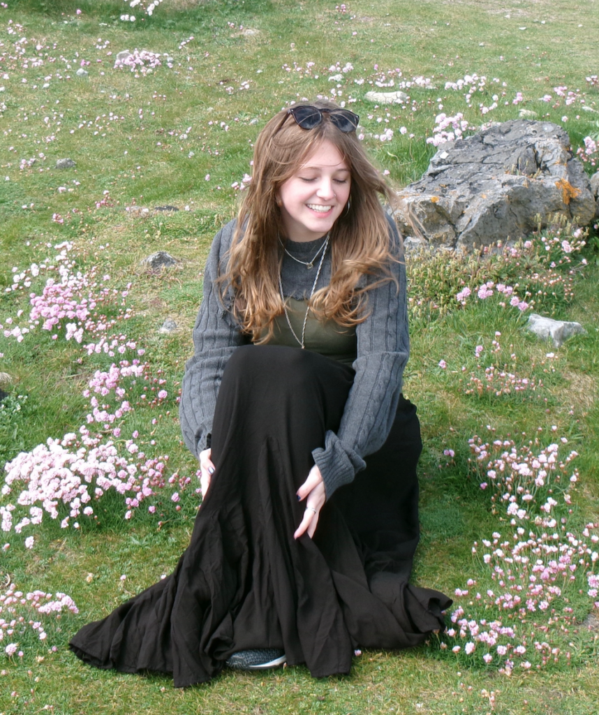 Lucy, sitting in a field by some rocks, smiling.
