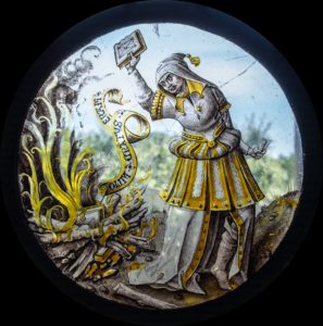 Early modern stained glass image of a figure in a cloak and hat burning books in a bonfire.